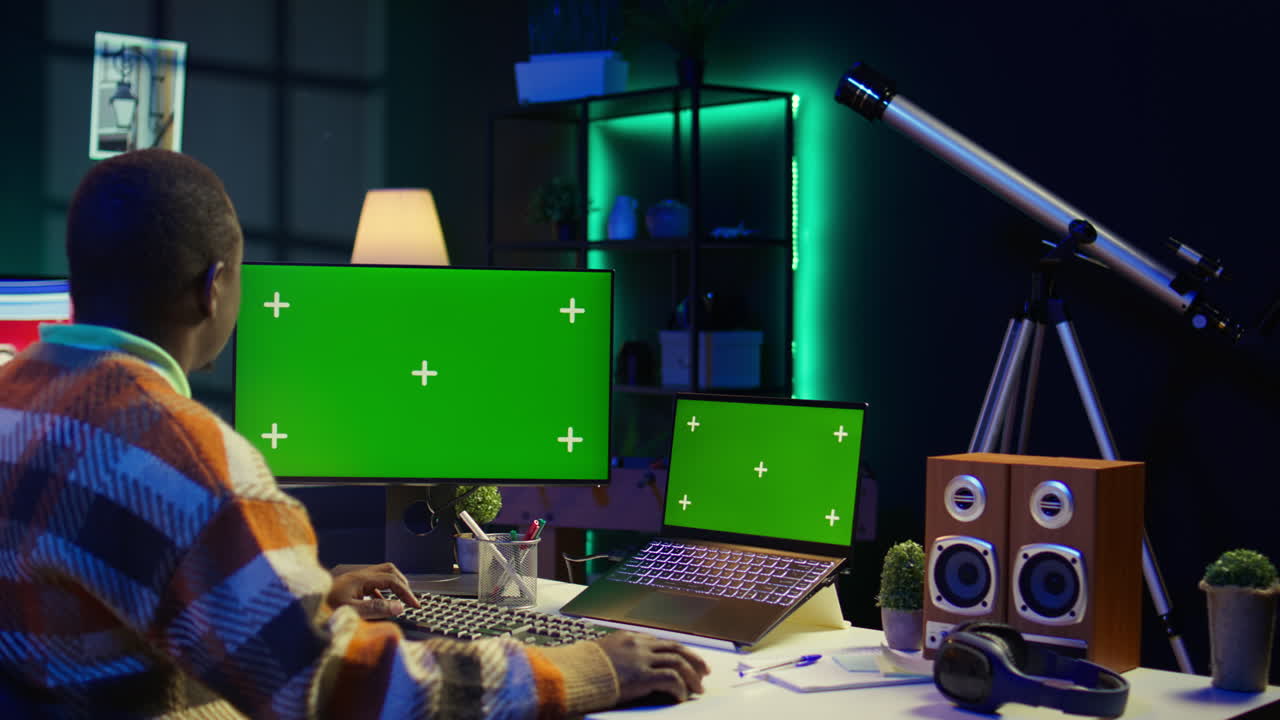 Man working at desk with computer and laptop with green screens
