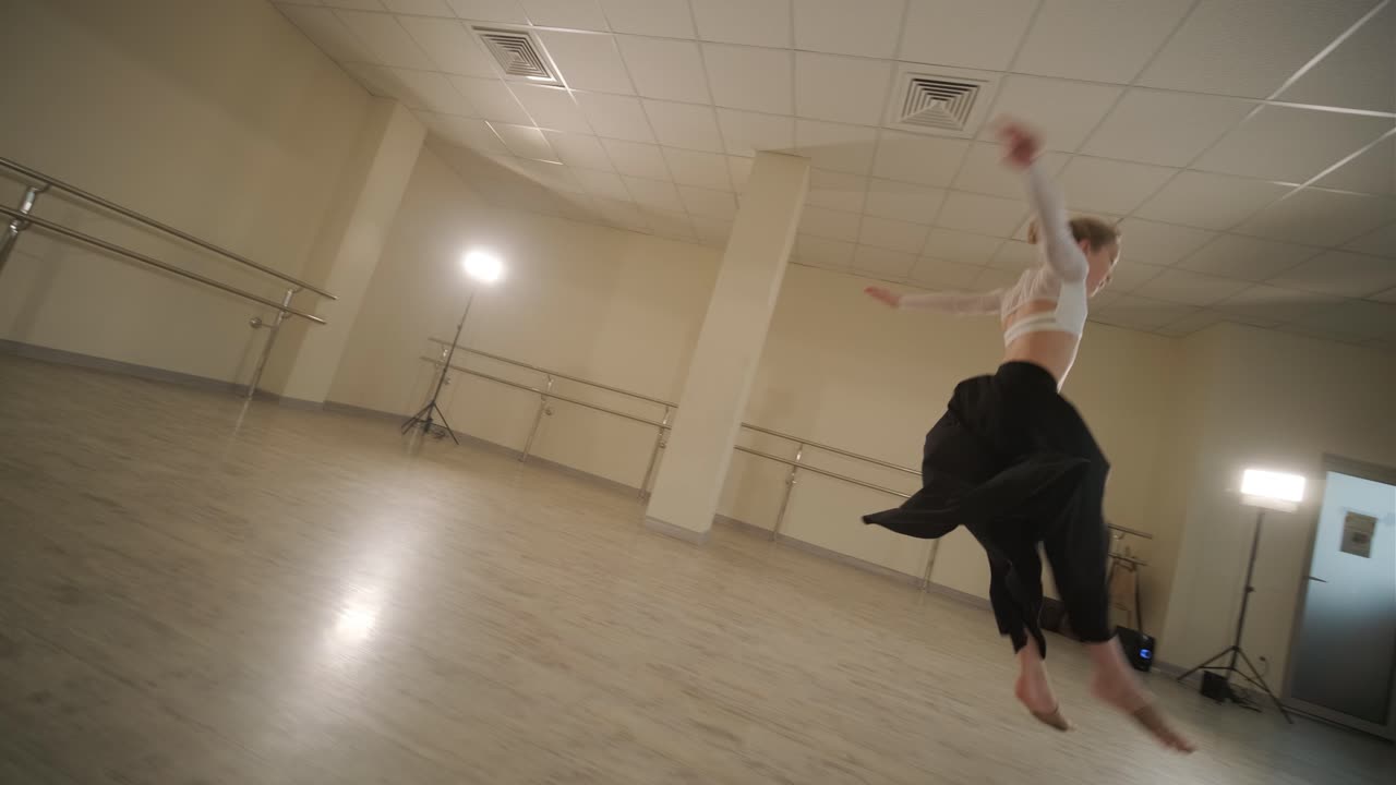 un grupo de jóvenes estudiantes de ballet con ropa de baile negra practicando posiciones en un amplio estudio de ballet con pisos de madera y barras montadas en la pared. expresiones enfocadas y movimientos sincronizados.