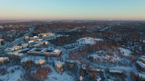 an aerial drone shot that slowly rises upwards while panning toward the left to reveal views of a densely populated urban city covered in sparkling white snow during winter