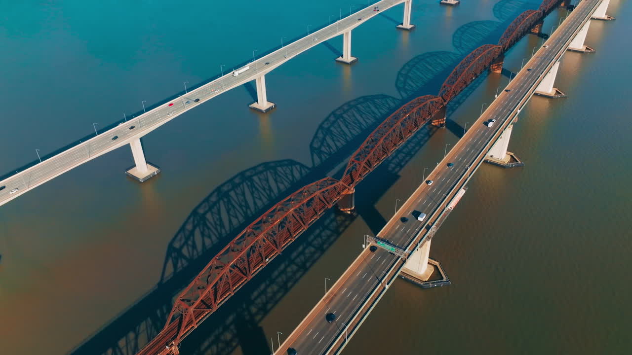 Beautiful simple bridges with one-way highways. Multiple cars moving by the bridges. Metal arched railway bridge in the middle.