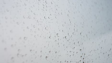 a close-up shot of heavy rain drops is seen through a window glass