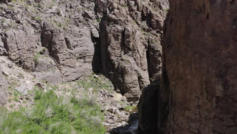 Aerial-view-of-a-narrow-canyon-with-a-river-flowing-below-and-towering-cliffs