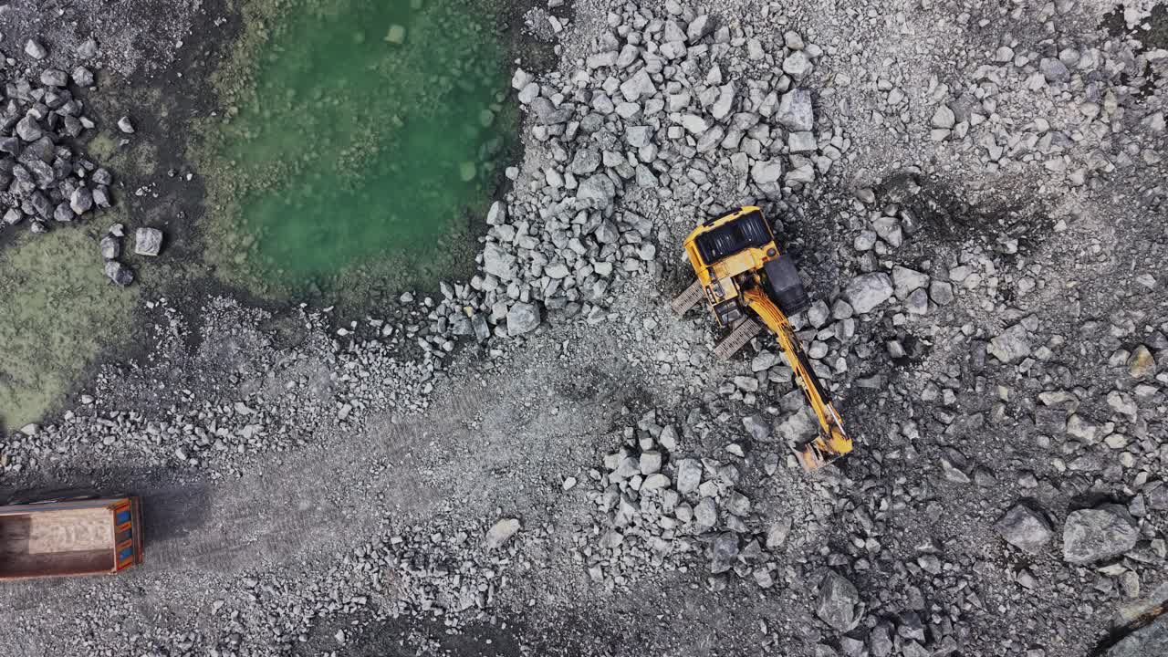 Luftfoto af dumper, der kører forbi en gravemaskine i et stenbrud.