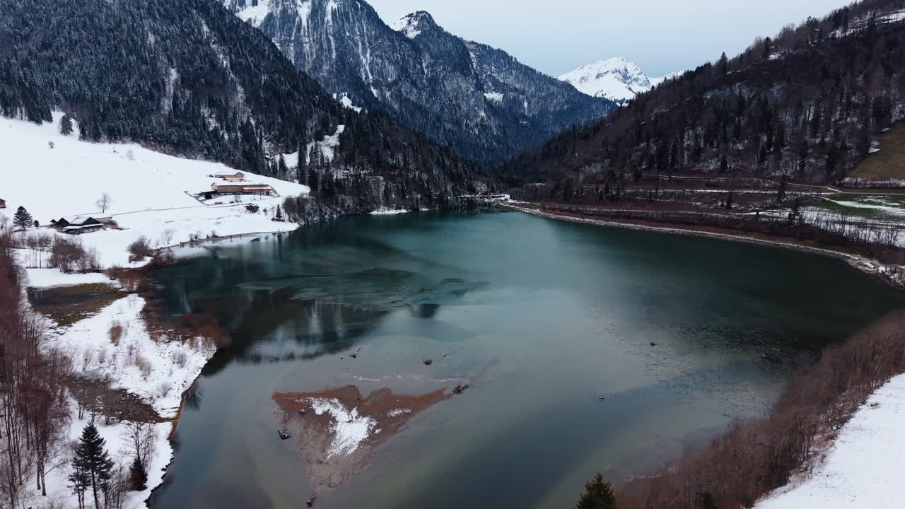 Aerea: Lago Vernex con neve e diga sullo sfondo in inverno a Rossiniere, distretto di Riviera-Pays-d'Enhaut, cantone di Vaud, Svizzera, ripresa con drone in allontanamento.