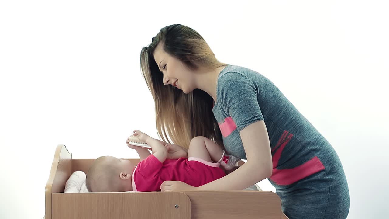 예쁜 젊은 어머니가 아기의 머리카락을  ⁇ 고 있습니다.