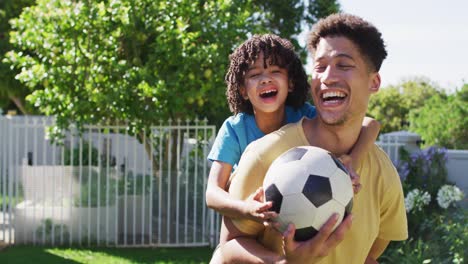 Porträt-Eines-Glücklichen-Gemischtrassigen-Mannes-Und-Seines-Sohnes,-Der-Im-Garten-Fußball-Spielt