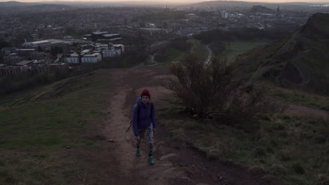 Dolly-Aufnahme-Eines-Mädchens,-Das-Abends-Während-Der-Goldenen-Stunde-Auf-Dem-Wanderweg-Den-Arthurs-Seat-Mountain-Hinaufgeht,-Mit-Der-Stadt-Edinburgh-Im-Hintergrund