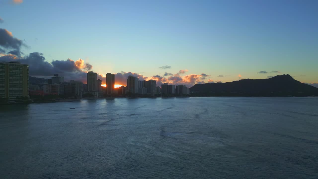 Beautiful and scenic dolly drone panoramic shot of Waikiki Beach, Hawaii, at sunset with the sun behind the clouds