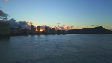 beautiful and scenic dolly drone panoramic shot of waikiki beach, hawaii, at sunset with the sun behind the clouds