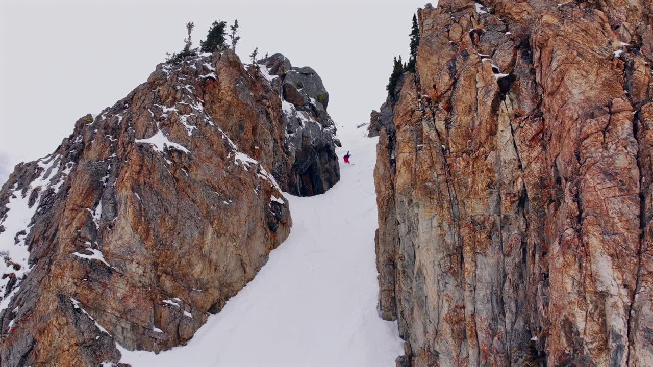 Snowboarder turning down Colorado chute Deer Creek Montezuma Loveland Pass deep powder backcountry avalanche terrain winter spring sunny rock walls aerial drone follow