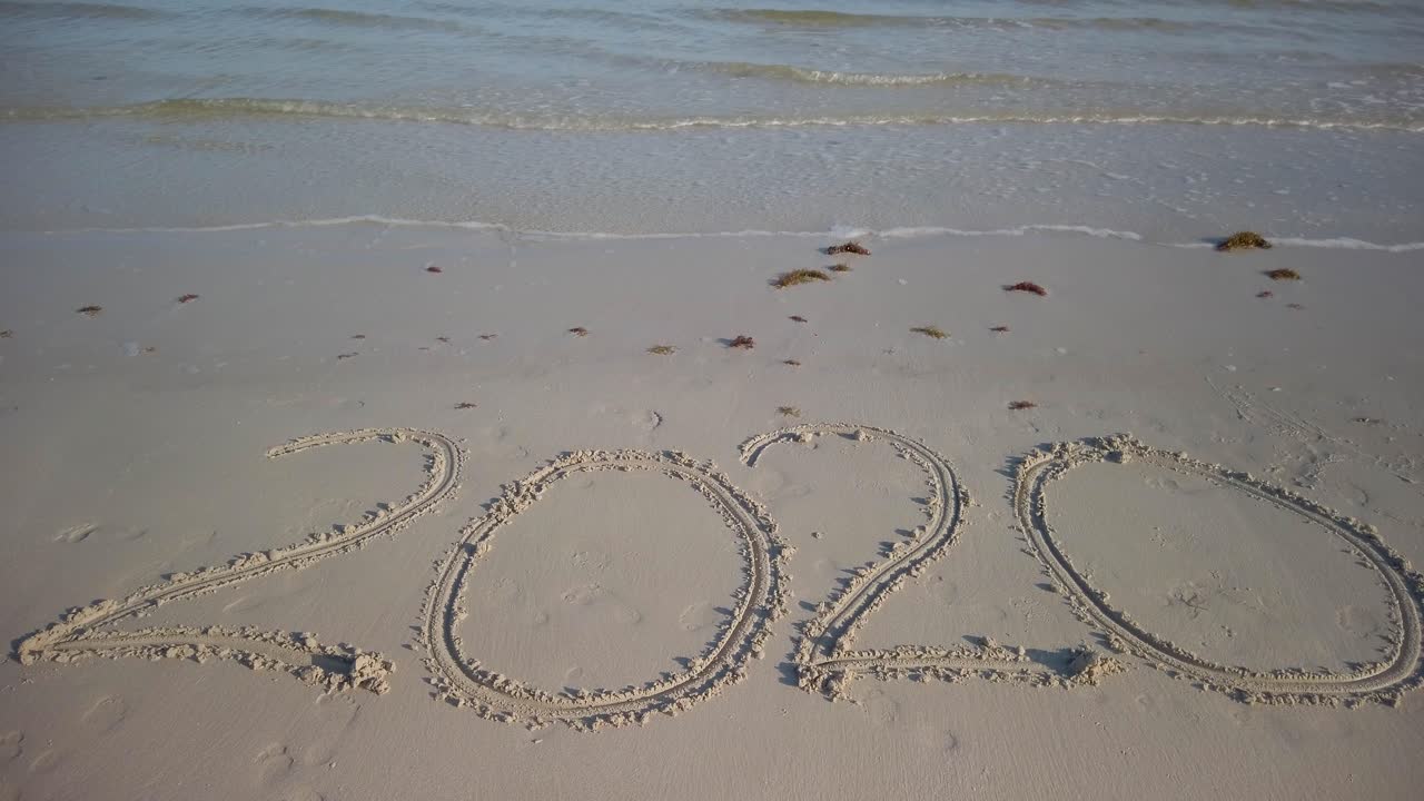 해변에 물이 찰랑이는 모래에 크게 쓰여진 2020년