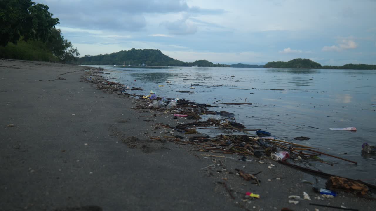 Slow-motion wide shot of rubbish on the ocean shore with islands in the background in Lombok, Indonesia