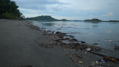 slow-motion wide shot of rubbish on the ocean shore with islands in the background in lombok, indonesia