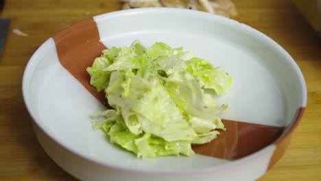 adding caesar salad mix into deep plate on wooden cut board in kitchen