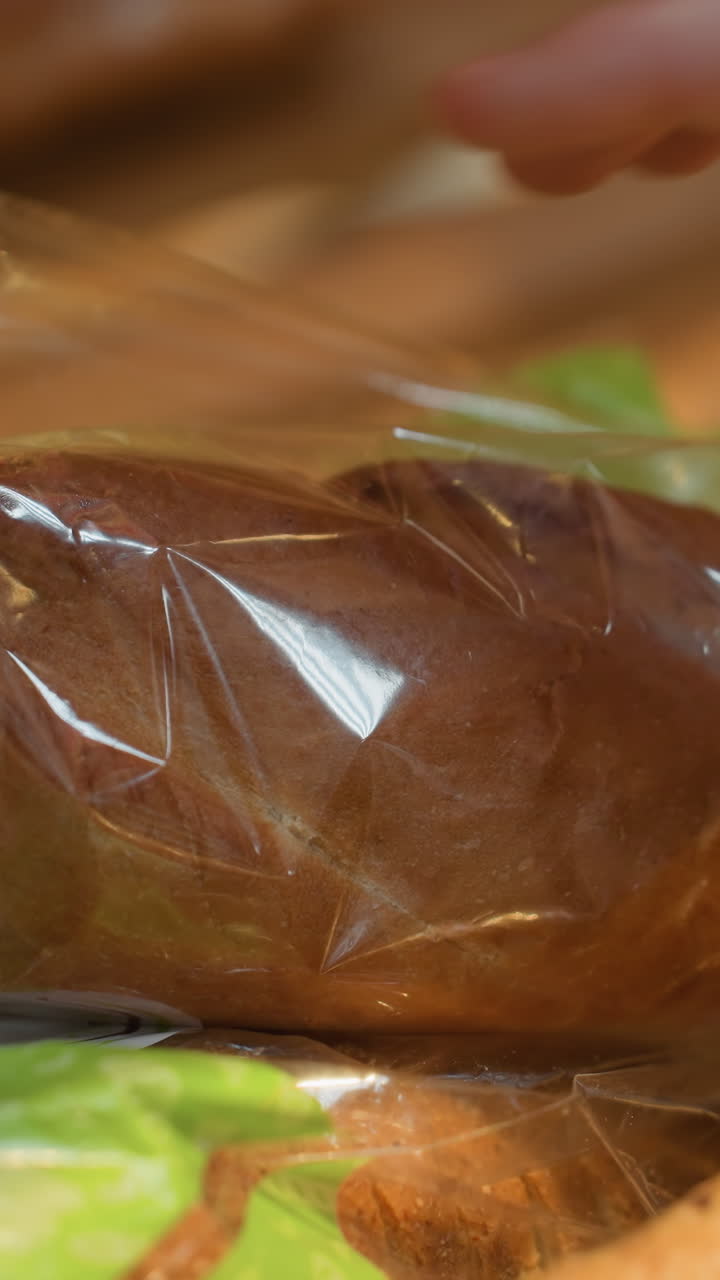 두 개의 구슬 팔를 착용 한 손이 식료품 가게에서  한 어리를 만지고 집어 들고, 휴대용 카메라로 촬영하여 베이커리 섹션에서 과 상세한 상호 작용을 포착합니다.