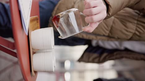 Vertical, person pours the last drops of coffee into white clay cups on table