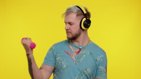 sporty tourist adult man listening music via headphones, working out, pumping up lifting dumbbells