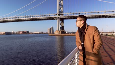 young asian korean tourist man in brown coat looking at the beautiful calm river in new jersey during sunset - close up shot