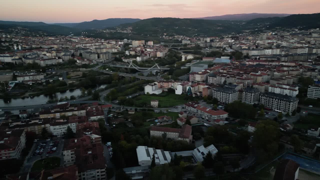 Aerial static pan across dense city of Ourense Spain at sunset along river