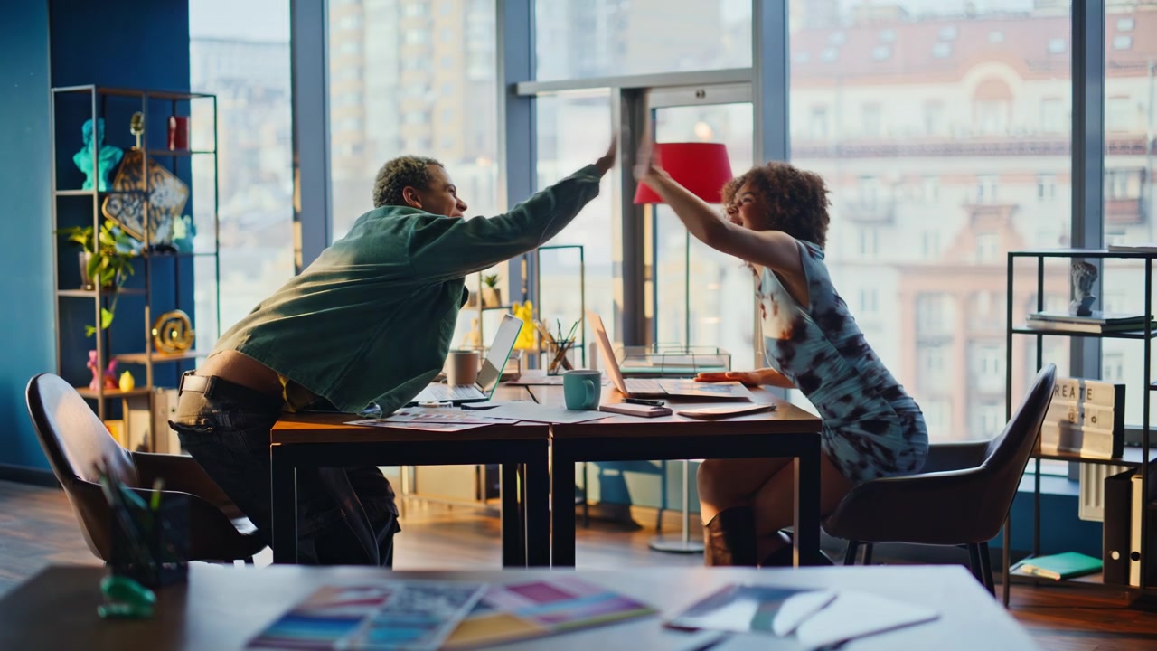 Two young colleagues brainstorming, celebrating high five in creative office
