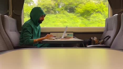 man in green hoodie using laptop on train while on the trip