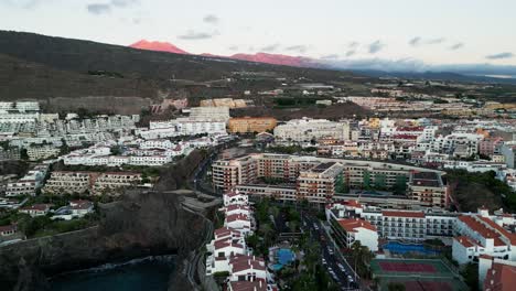 Die-Drohne-Fängt-Die-Stadt-Los-Gigantes-Mit-Ihrem-Malerischen-Küstencharme-Ein,-Während-In-Der-Ferne-Der-Majestätische-Rot-Gefärbte-Vulkan-Teide-Als-Wahrzeichen-Der-Insel-Teneriffa-Steht