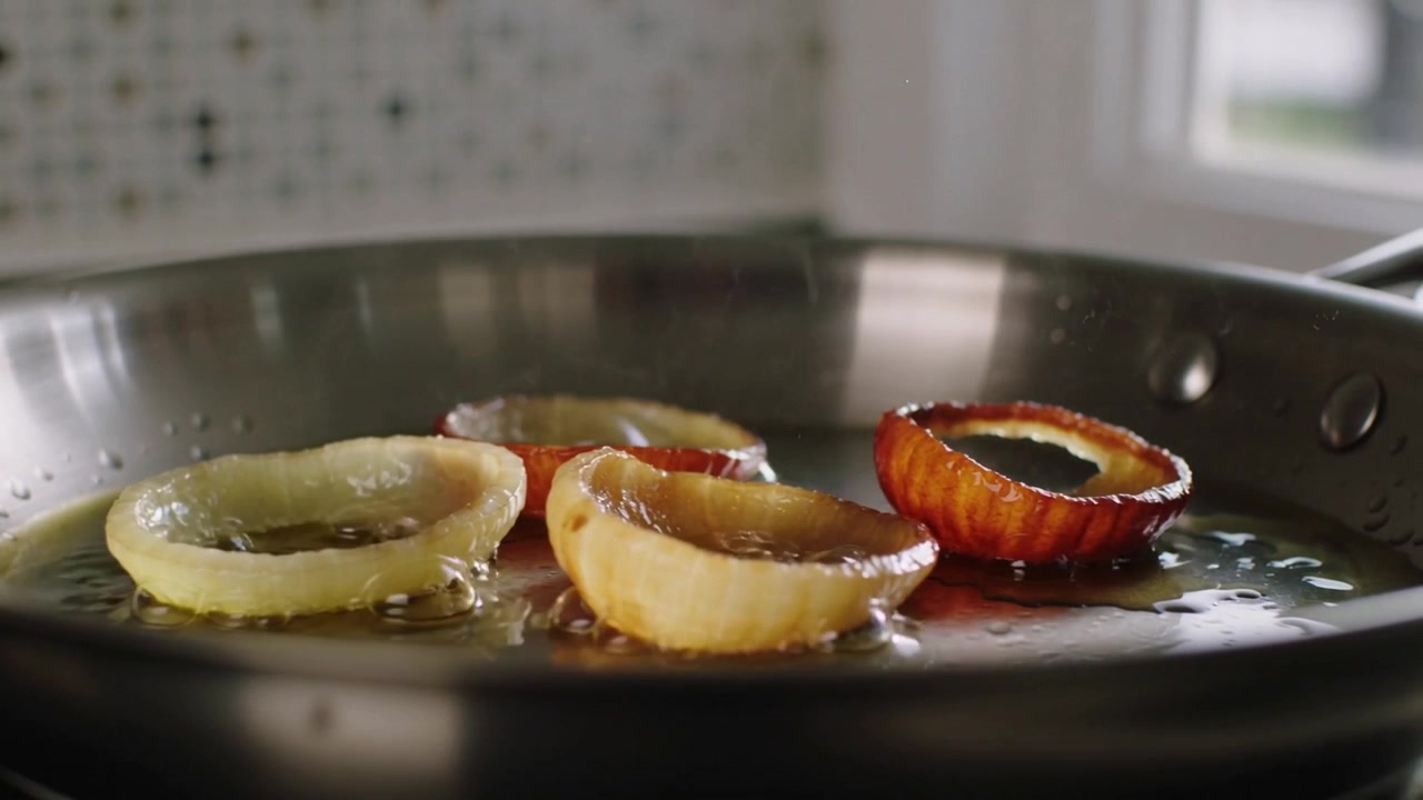 Frying thick onion rings browning on stovetop in steel skillet as oil shimmering, caramelizing