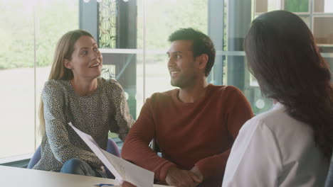 Female-Doctor-In-Office-Discussing-Test-Results-With-Smiling-And-Relieved-Couple-In-Hospital