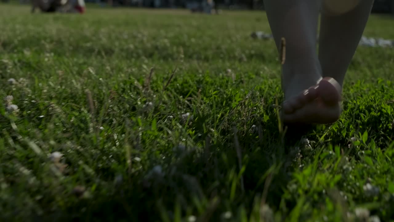 Slow-motion of a woman walking barefooted on the grass towards the following camera on a sunny summer day
