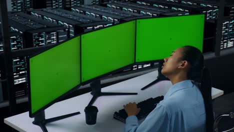 side view of tired asian woman stretching while working with mock up multiple computer monitor in data center