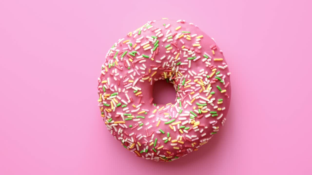 Vista superior de donut rosa com cobertura e confeitos girando isolado. Filmado com câmera RED em 4K.