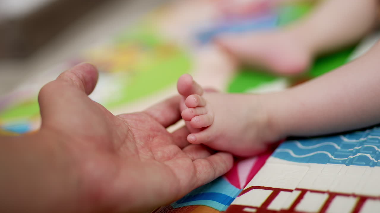 Daddy's hand holds little baby foot. Father caresses kid's tiny fingers and child moves his fingers slowly. Close up. Blurred backdrop.