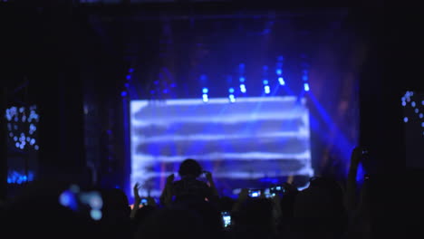 a slow motion of a crowd in front of the bright stage at an open air concert