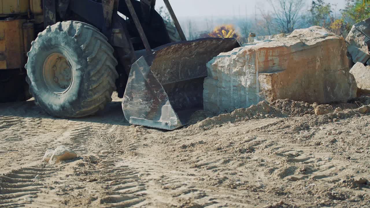An old bulldozer moves a large stone on a quarry. Close-up