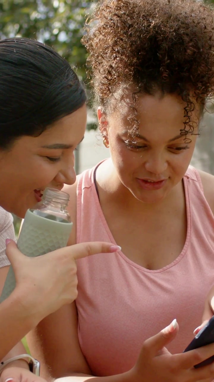 Vertical video: Opening bottle, pair with one in pink tank sipping, viewing phone after tap on lawn