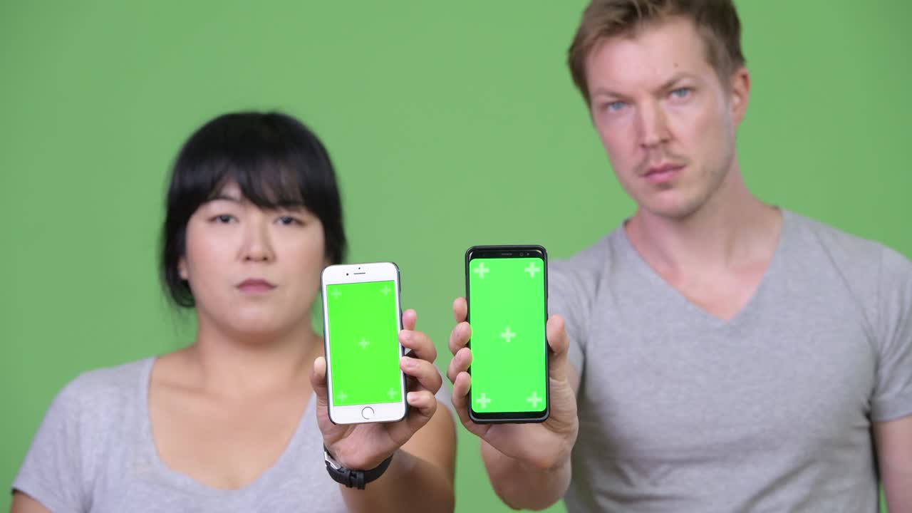 Young happy multi-ethnic couple showing two phones together