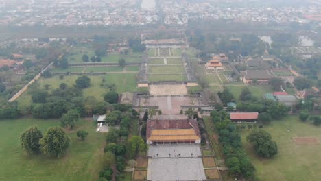 Drone-aerial-view-in-Vietnam-flying-over-Hue-imperial-stone-brick-fortress-wall,-green-gardens,-temples-and-small-buildings-on-a-cloudy-and-foggy-day