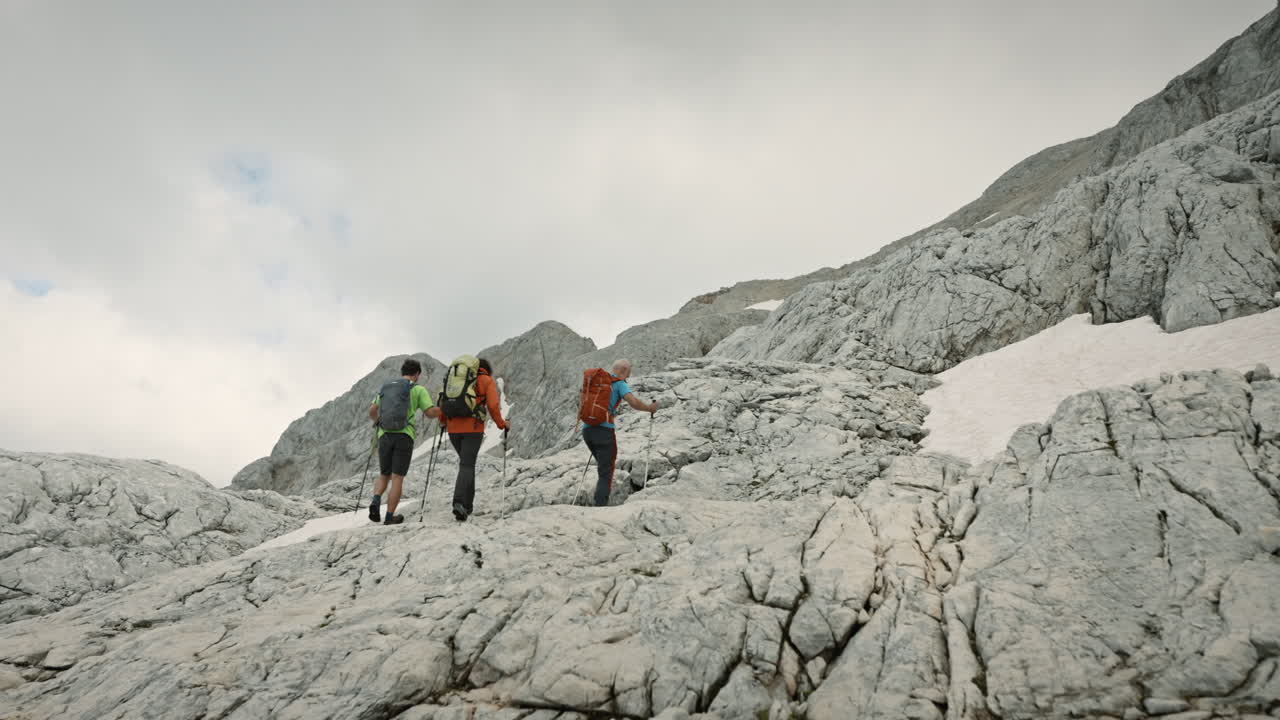 Hikers waring backpacks and using hiking poles to help with walking on the incline, climbing on rocks of a mountain