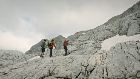 Excursionistas-Con-Mochilas-Y-Usando-Bastones-De-Senderismo-Para-Ayudar-A-Caminar-En-La-Pendiente,-Escalar-Rocas-De-Una-Montaña