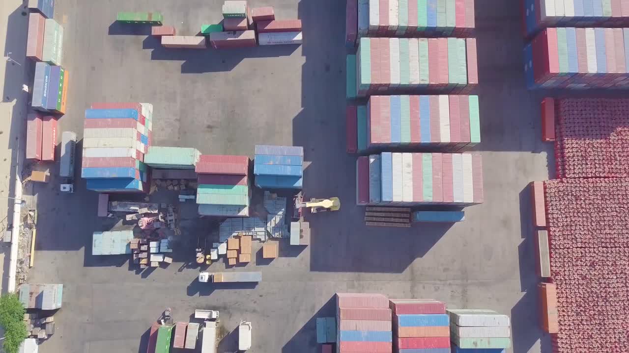 Vertical pan of a very large gated container yard with trucks, a forklift, and a cargo carrier