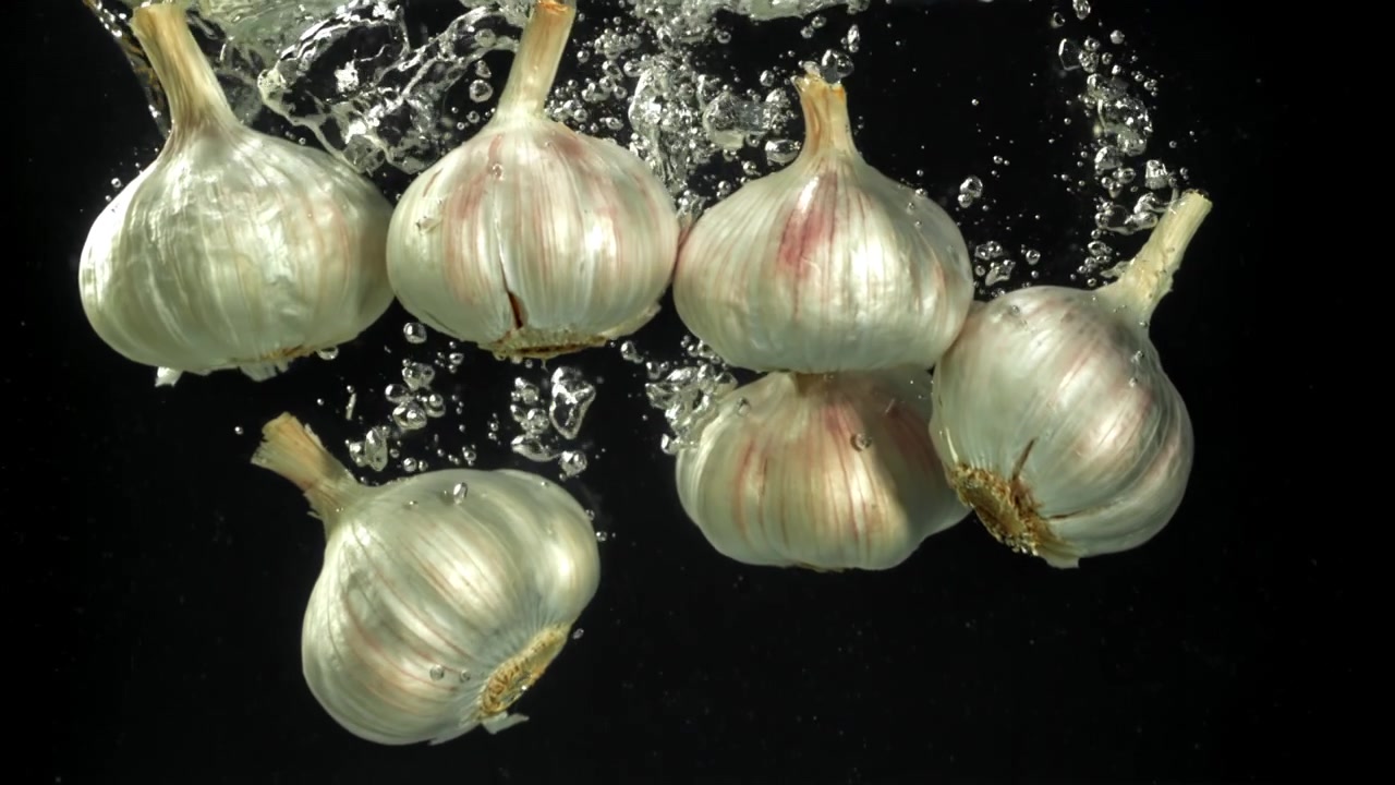 Bulbi d'aglio freschi che cadono nell'acqua con bolle su sfondo nero