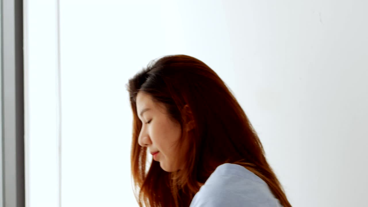 젊은 아시아 여성이 스마트폰과 신용카드를 가지고 집 창문 에서 미소 짓고 있습니다. 아름다운 여성이 신용카드로 온라인으로 쇼핑하고 있습니다.