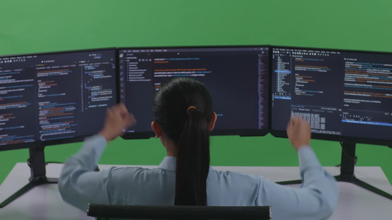 Back View Of Happy Asian Woman Developer Celebrating While Write Code With Multiple Computer Screens In Green Screen Studio