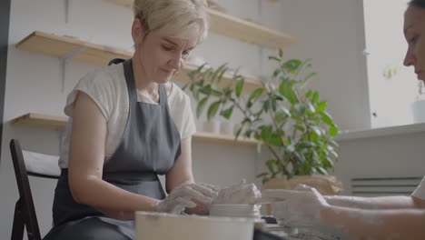 a female potter's wheel sculpting teacher explains how to work and teaches an elderly woman to work with clay and make mugs and jugs. master class for pensioners. pottery courses