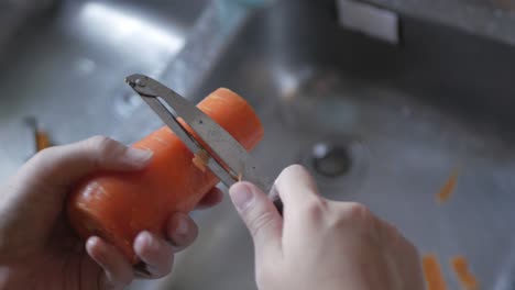 close-up of hands while peeling fresh juicy carrot by peeler