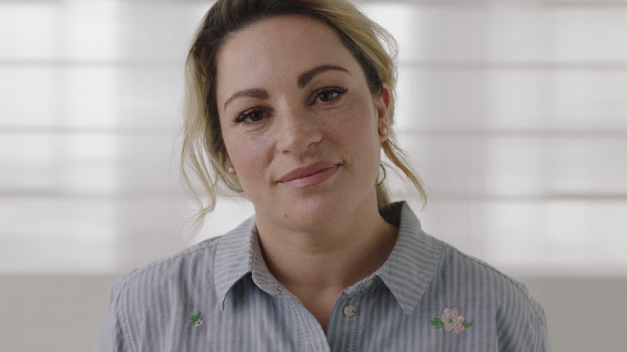 retrato de cerca de una joven rubia sonriendo mirando a la cámara corriendo de la mano a través del cabello con una camisa casual