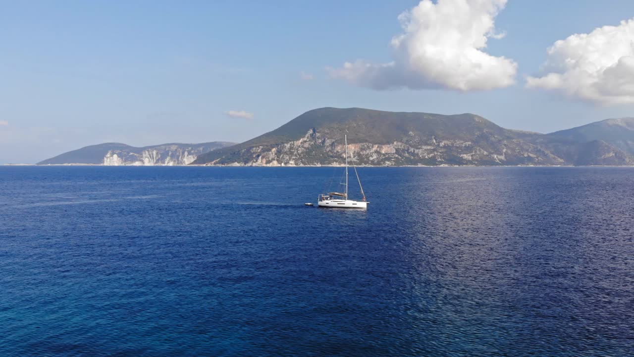 Barca che naviga nell'oceano blu in una giornata nuvolosa con vista sul versante montuoso di Paralia Emplisi Cefalonia, Grecia - Ripresa aerea laterale.