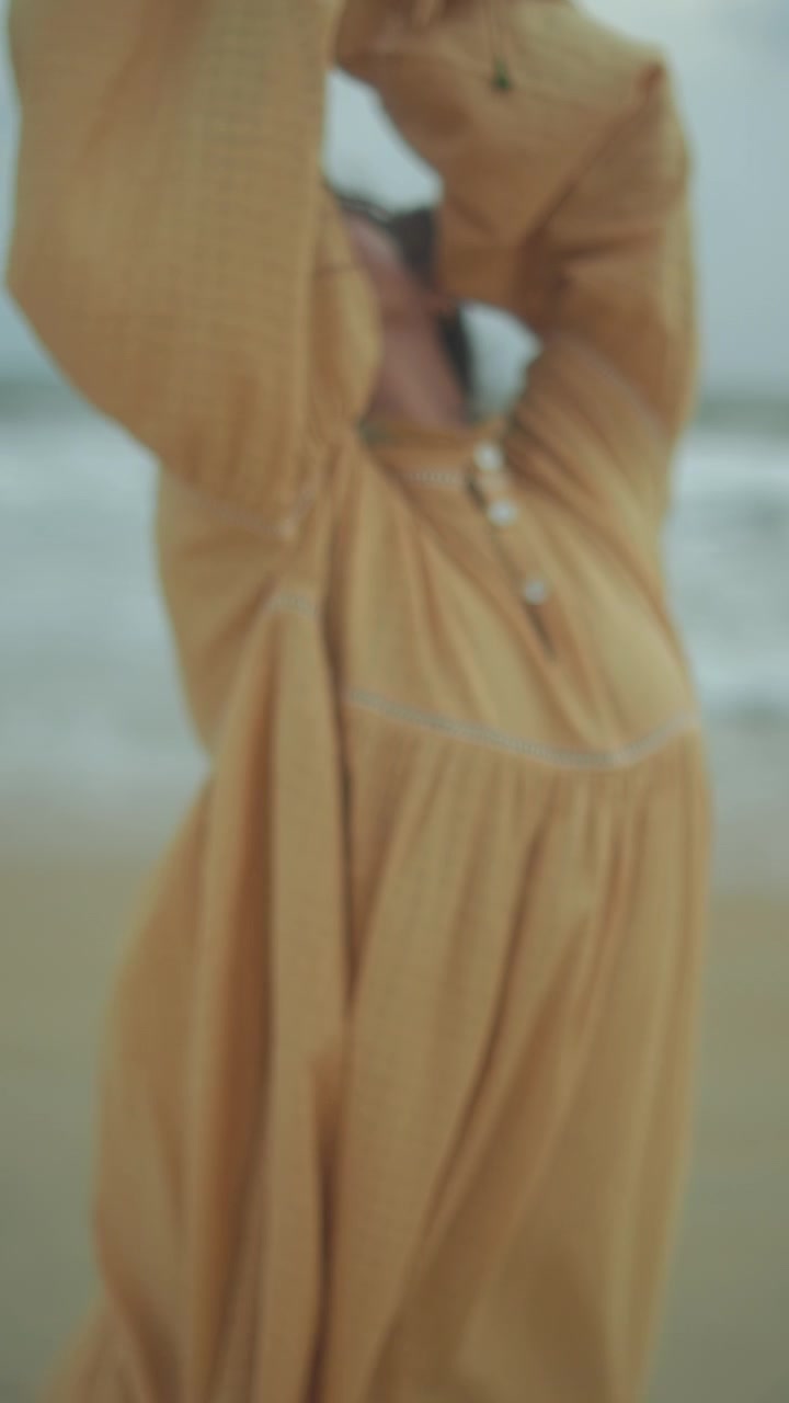 Donna in abito giallo ampio che si muove con grazia su una spiaggia sabbiosa vicino alle onde dell'oceano.