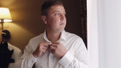 stylish man in jacket fastens buttons, buttoning white shirt preparing to go out near window