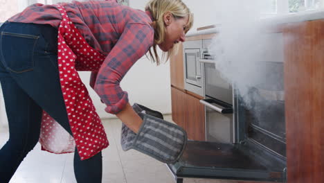 mujer madura en la cocina toma la comida ardiendo del horno